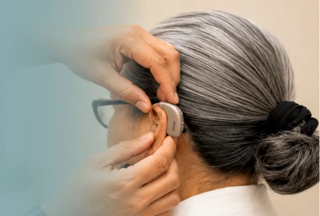 Profesional colocando un audífono retroauricular detrás de la oreja de una paciente en SEBI Centro Audiológico